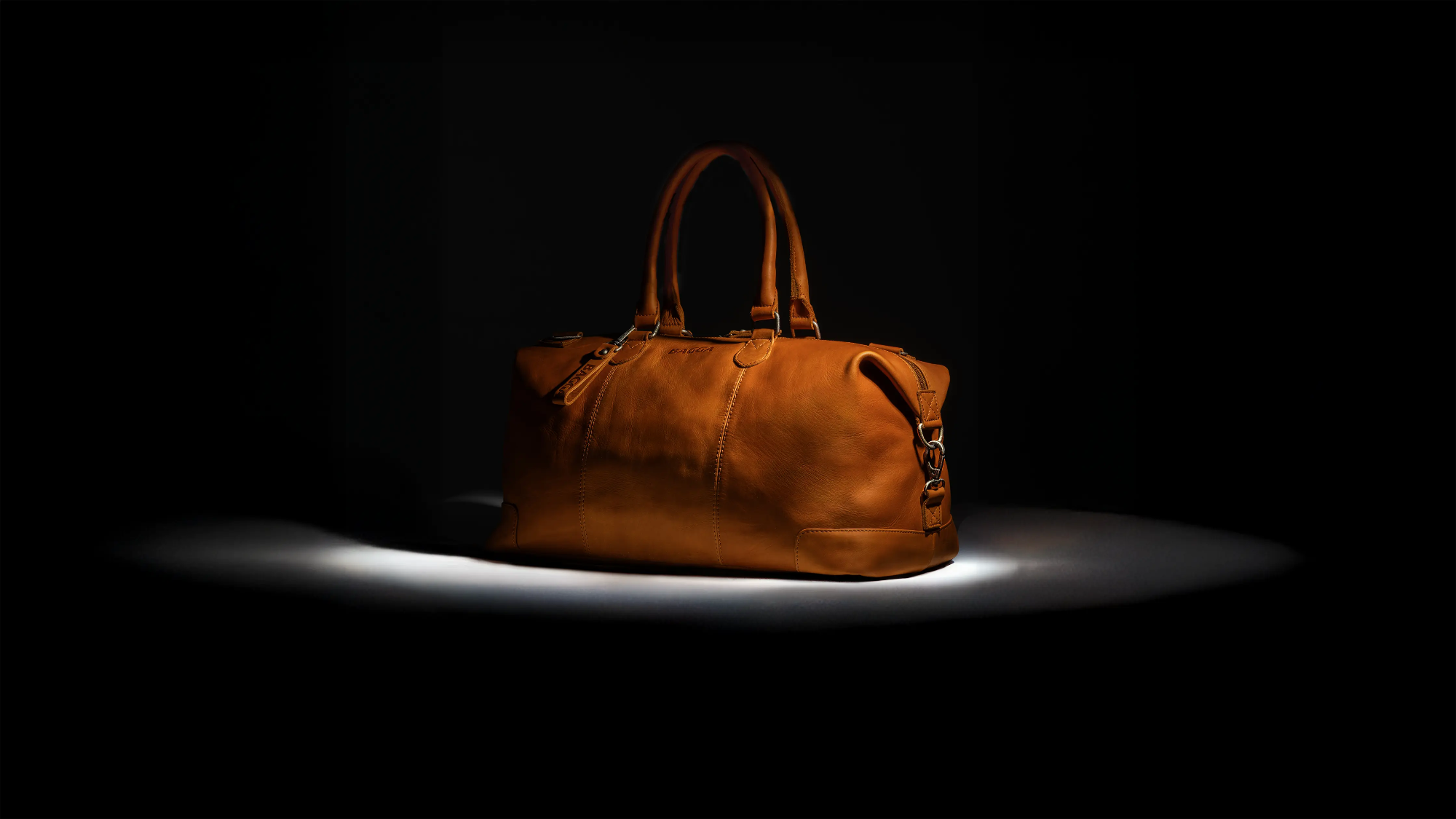 Cognac leren weekendtas van Bagga met dubbele handgrepen op zwarte achtergrond